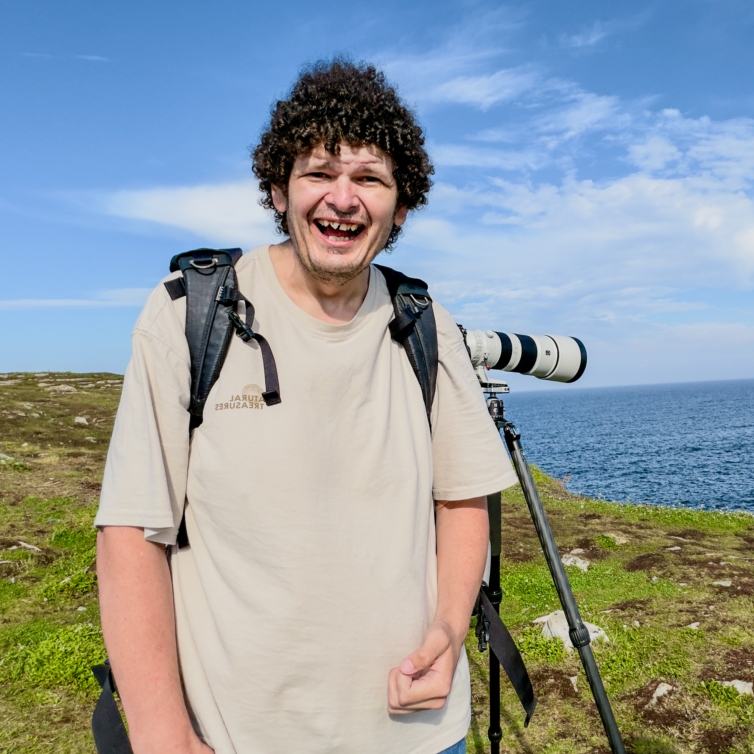 Ben is stood atop a cliff edge on the North Atlantic coast, pictured with a large grin beside his camera setup
