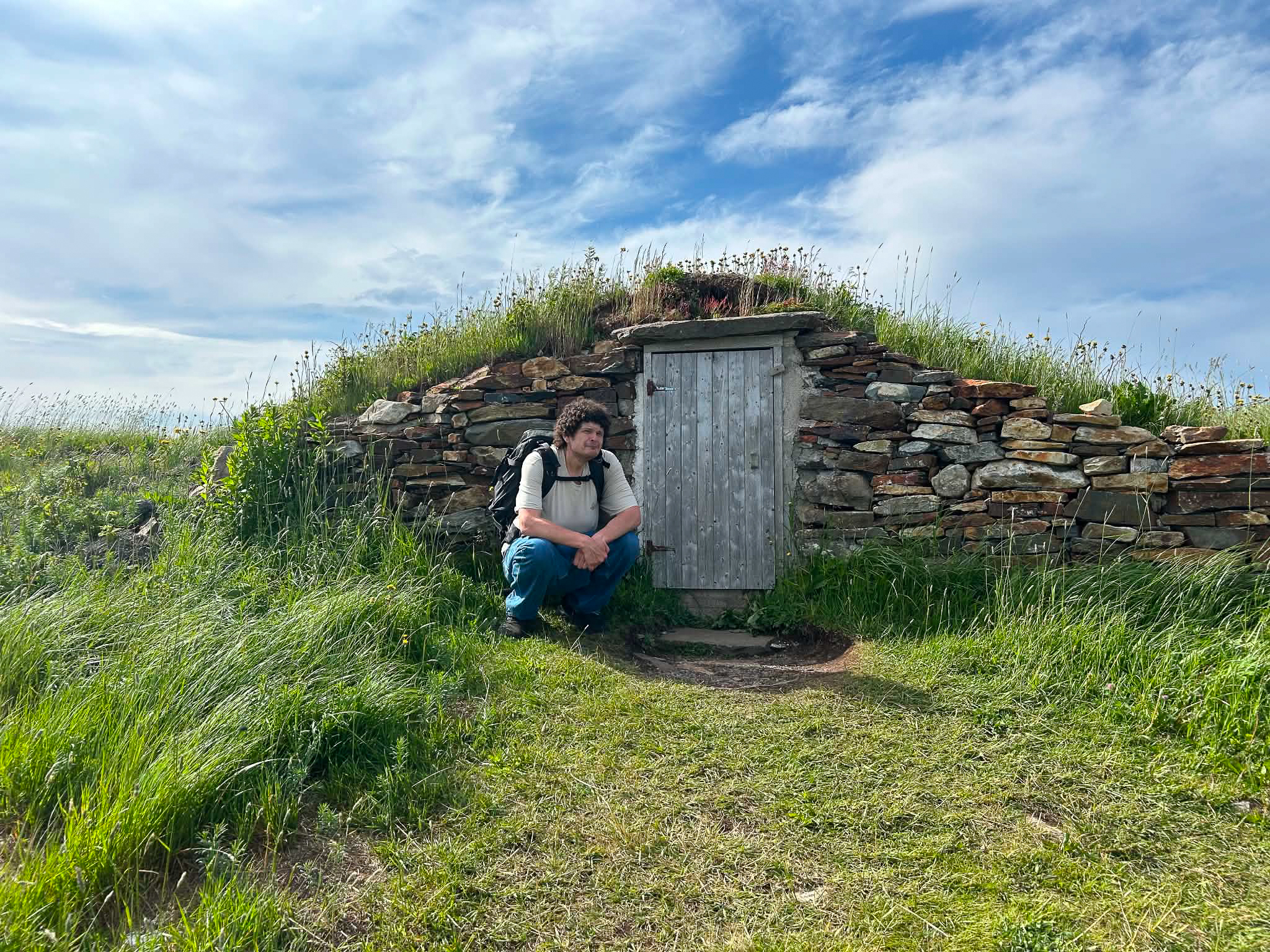 Ben is pictured crouched beside a wooden door set into a stone-faced mound, one of the famous Root Cellars of Elliston
